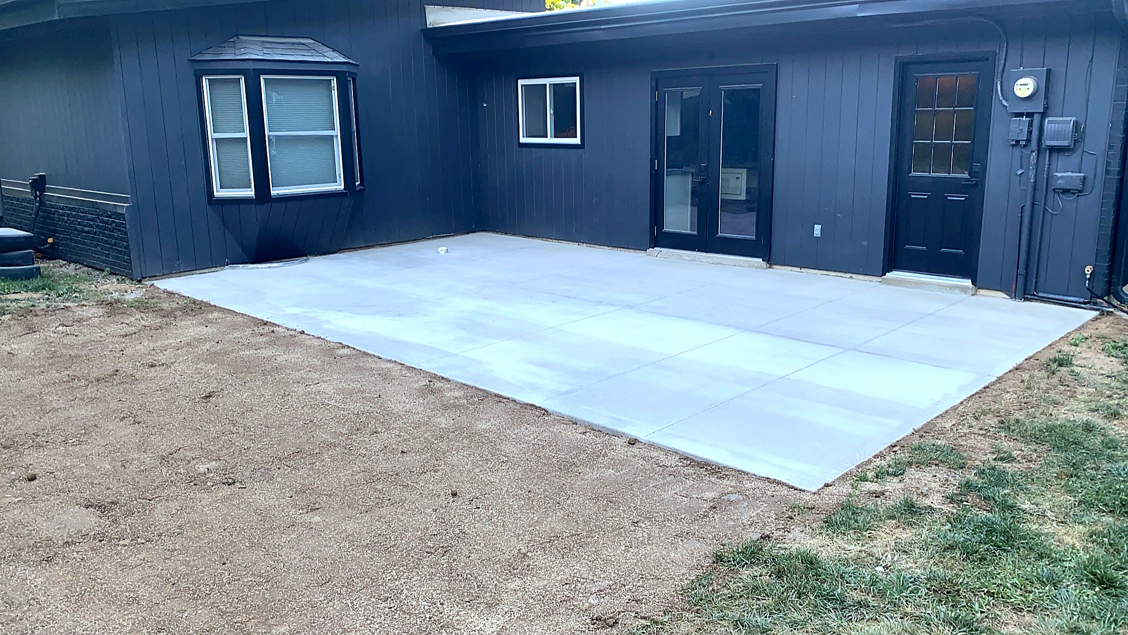 Concrete patio behind modern dark-sided home
